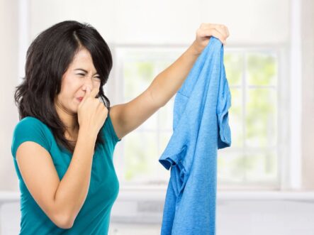woman pinching her nose and holding a smelly shirt in her hand.